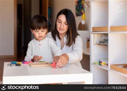 Lillte Kid playing with a tetris wood puzzle and mother or teacher help. Homeshooling. Learning Community. Montessori School