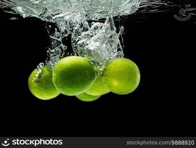 Lime Citrus Fruits splashing with bubbles into water isolated against black background. Citrus theme.. Lime Citrus Fruits splashing with bubbles into water isolated against black background