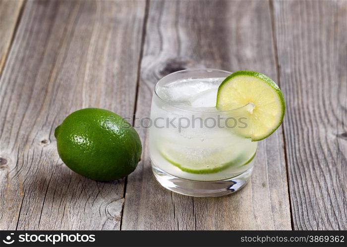 Lime drink, focus on lip of glass and lime slice, with whole lime on rustic wood.