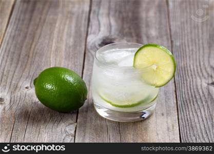 Lime drink, focus on lip of glass and lime slice, with whole lime on rustic wood.
