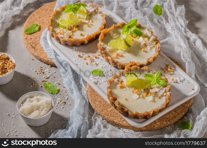 Lime vegan tarts with grated coconut and crunchy peanuts. Citrus cake. Date, walnut, almond and hazelnut base.