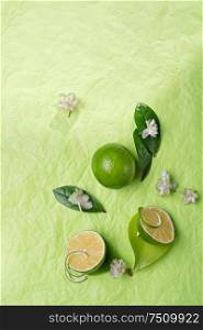 limes with leaves and flowers on green background. flat lay. copy space