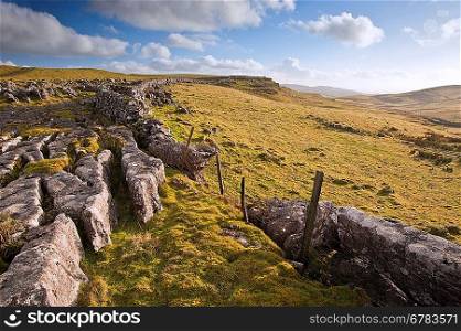 Limestone rocks and flint walls lead towards Malham Moor in distance in Yorkshire Dales National Park