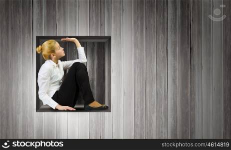 Limited and restricted. Young woman trapped in wooden cube in wall