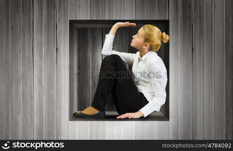 Limited and restricted. Young woman trapped in wooden cube in wall