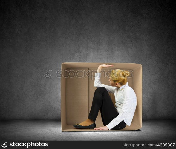 Limited possibilities. Young businesswoman sitting in carton box and feeling uncomfortable