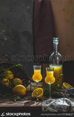 Limoncello in grappas wineglass with water drops and lavender on dark wooden table. Artistic still life on dark background with sunny light.