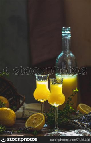 Limoncello in grappas wineglass with water drops and lavender on dark wooden table. Artistic still life on dark background with sunny light.