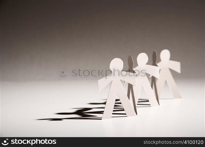 Line of cutout paper dolls throwing a shadow