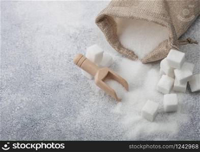 Linen bag of natural white refined sugar with cubes and wooden spoon on light background.