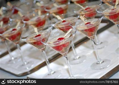 Lines of glasses filled with champagne and two raspberries on a stick, photographed with a shallow depth of field