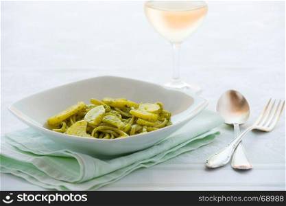 Linguine pasta with pesto genovese and potatoes over a table with cutlery and white wine glass. Linguine pasta with pesto genovese and potatoes