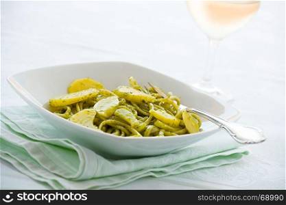 Linguine pasta with pesto genovese and potatoes over a table with fork and white wine glass. Linguine pasta with pesto genovese and potatoes