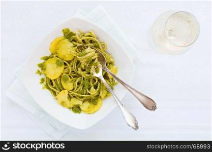 Linguine pasta with pesto genovese, potatoes and white wine glass seen from above. Linguine pasta with pesto genovese, potatoes and white wine glass
