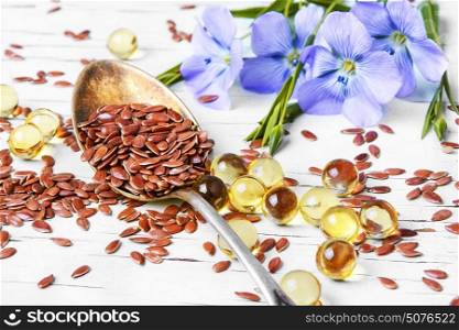 Linseed on wooden background. Spoon with flax seeds and capsules with linseed oil