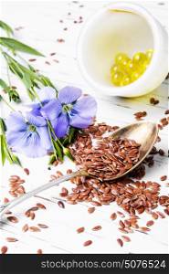 Linseed on wooden background. Spoon with flax seeds and capsules with linseed oil