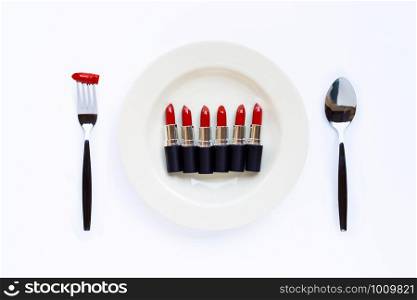 Lipsticks on white dish with fork and spoon on white background.