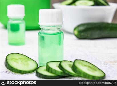 Liquid cosmetics skin care in a bottle and green cucumber with a slice of cucumber on a white wooden table. Natural extract from cucumber. Spa. Liquid cosmetics skin care in a bottle and green cucumber with a slice of cucumber on a white wooden table. Natural extract from cucumber.