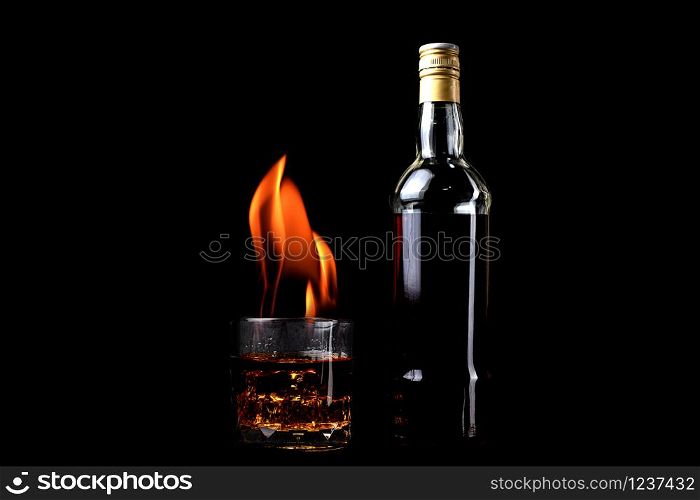 Liquor bottles and whiskey glass with and fire flame on black background