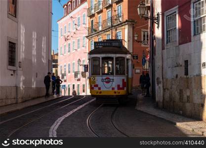 Lisbon, Portugal - March 23, 2019: Yellow tram, symbol of Lisbon at sunny street with walking tourists
