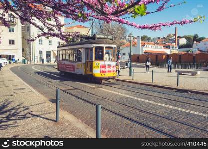Lisbon, Portugal - March 23, 2019: Yellow tram, symbol of Lisbon at sunny street with walking tourists