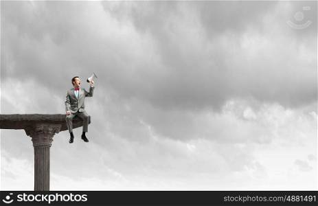 Listen everyone. Businessman sitting on top edge and screaming in megaphone