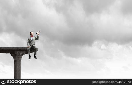 Listen everyone. Businessman sitting on top edge and screaming in megaphone