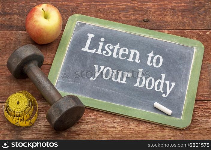 Listen to your body concept - slate blackboard sign against weathered red painted barn wood with a dumbbell, apple and tape measure