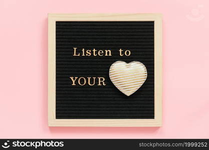 Listen to your heart. Motivational quote in gold letters and decorative textile heart on black letter board on pink background. Top view Flat lay Concept inspirational quote of the day.. Listen to your heart. Motivational quote in gold letters and decorative textile heart on black letter board on pink background. Top view Flat lay Concept inspirational quote of the day