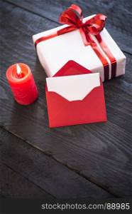 Lit candle red envelope with blank paper, leaned against an elegantly wrapped gift box, decorated with a red ribbon bow.