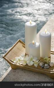 Lit pillar candles on tray with white orchids beside pool.