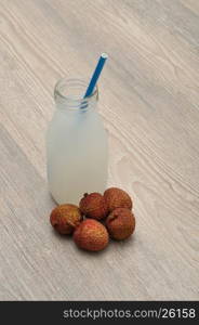 Litchi juice in a glass bottle with a blue straw and fresh litchis .