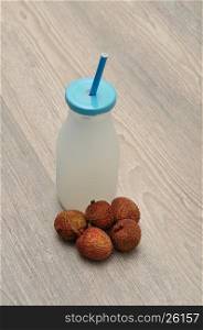 Litchi juice in a glass bottle with a blue straw and lid and fresh litchis
