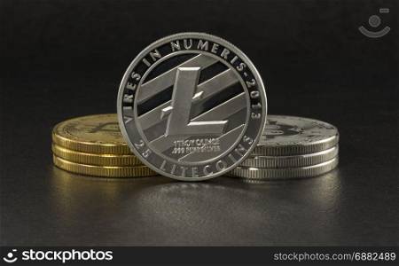 litecoin and bitcoin with black background with a single litecoin facing the camera in sharp focus with shading on the icon letter B on the face of the bit coin