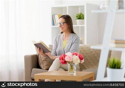 literature, education and people concept - happy middle-aged woman in glasses reading book at home. happy woman in glasses reading book at home