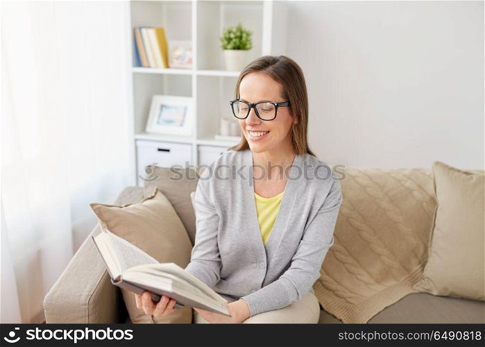 literature, education and people concept - happy middle-aged woman in glasses reading book at home. happy woman in glasses reading book at home. happy woman in glasses reading book at home