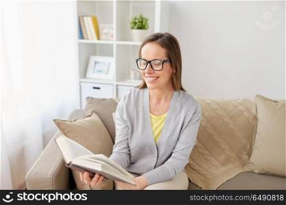 literature, education and people concept - happy middle-aged woman in glasses reading book at home. happy woman in glasses reading book at home. happy woman in glasses reading book at home