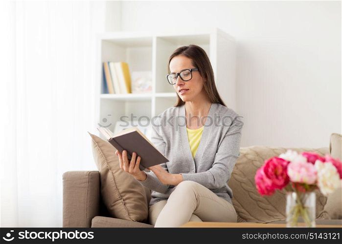 literature, education and people concept - young woman in glasses reading book at home. young woman in glasses reading book at home