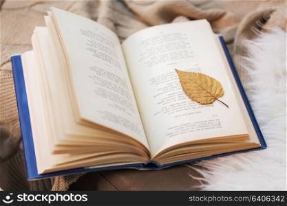 literature, reading and poetry concept - book with autumn leaf on blanket at home. book with autumn leaf on blanket at home