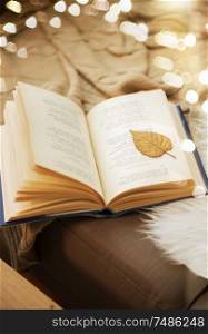 literature, reading and poetry concept - book with autumn leaf on page on sofa at home. book with autumn leaf on page on sofa at home
