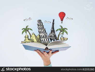 literature, travel and education concept - close up of woman hand holding open blue book with landmark drawing