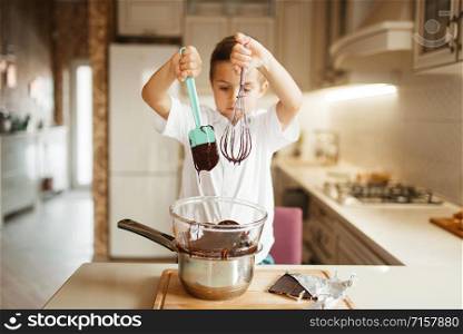 Litte boy stirs melted chocolate in a bowl. Kid cooking on the kitchen. Happy child prepares sweet dessert at the counter