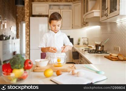 Litte boy stirs raw eggs in a bowl, pastry preparation. Kid cooking on the kitchen. Happy child prepares sweet dessert. Litte boy stirs raw eggs in a bowl
