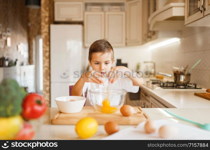 Litte boy stirs raw eggs in a bowl, pastry preparation. Kid cooking on the kitchen. Happy child prepares sweet dessert at the counter