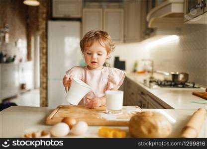 Litte girl pours milk into a glass, pastry with melted chocolate preparation. Kid cooking on the kitchen. Happy child prepares sweet dessert at the counter