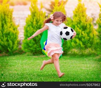 Little active football fan running on the green grass field with ball, young supporter of Brazilian football team with national flag