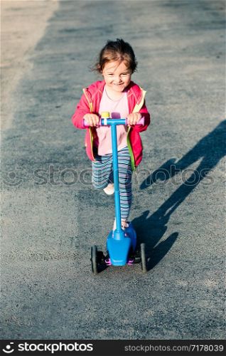 Little adorable girl having fun riding on scooter, playing outdoors