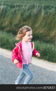 Little adorable girl having fun running on road, playing outdoors
