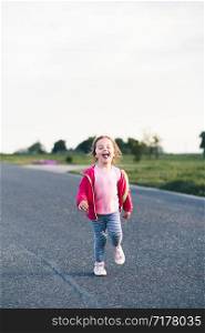 Little adorable girl having fun running on road, sticking her tongue out, playing outdoors