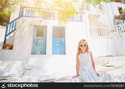Little adorable girl in dress outdoors in old streets an Mykonos. Kid at street of typical greek traditional village with white walls and colorful doors on Mykonos Island, in Greece. Little adorable girl in dress outdoors in old streets an Mykonos.